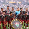 Jogadores do Fluminense posam para foto em campo, segurando o escudo do time, no Mundial de Clubes da FIFA 2025.