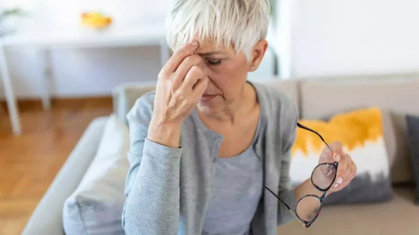 Mulher na menopausa com crise de enxaqueca, segurando a cabeça devido à dor intensa.