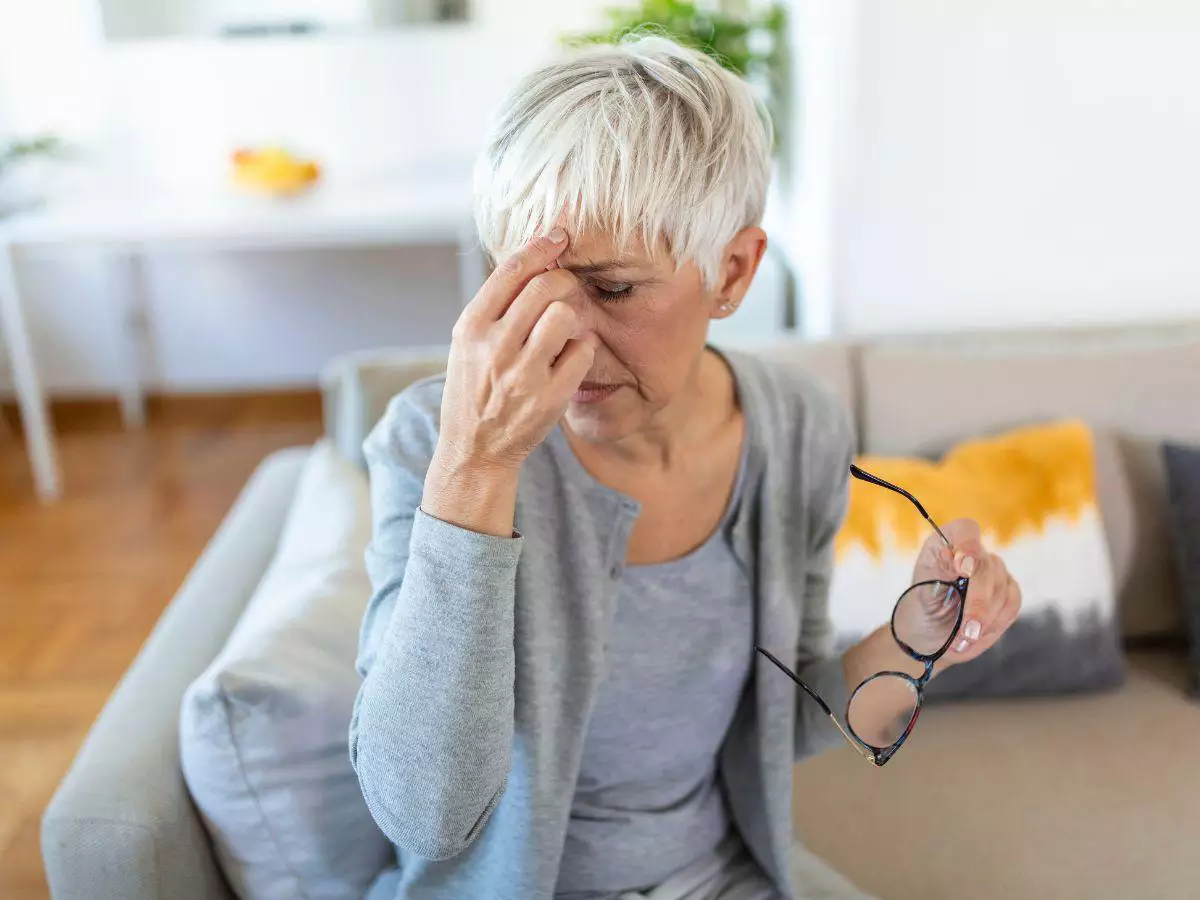 Mulher na menopausa com crise de enxaqueca, segurando a cabeça devido à dor intensa.