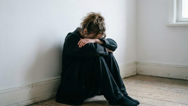 Mulher sentada no chão de pijama preto, com o rrosto encostado nas pernas.