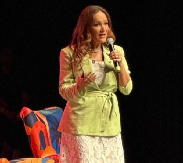 Pri de Sousa, no palco do Teatro Riachuelo, vestindo saia longa branca e Blazer verde, falando sobre Autoridade no marketing digital