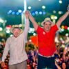 Lula e Cadu de Lula de mãos dadas para o alto com os eleitores ao fundo da foto