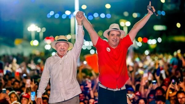 Lula e Cadu de Lula de mãos dadas para o alto com os eleitores ao fundo da foto