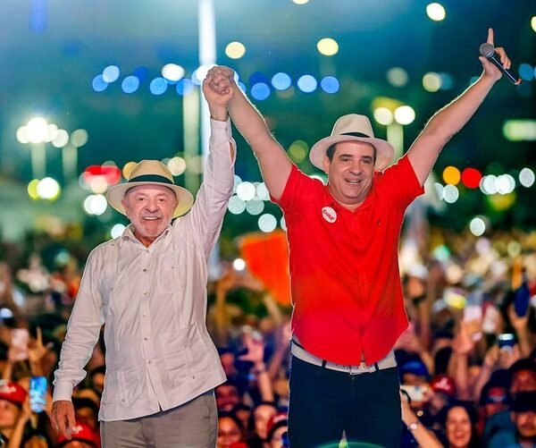 Lula e Cadu de Lula de mãos dadas para o alto com os eleitores ao fundo da foto
