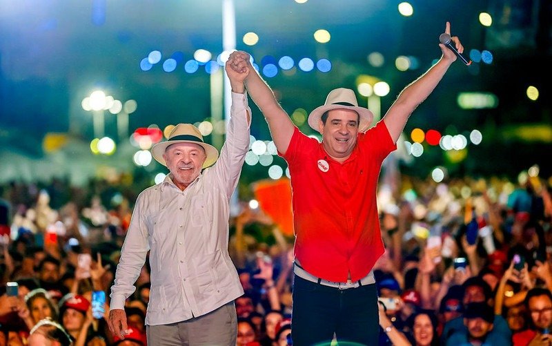 Lula e Cadu de Lula de mãos dadas para o alto com os eleitores ao fundo da foto